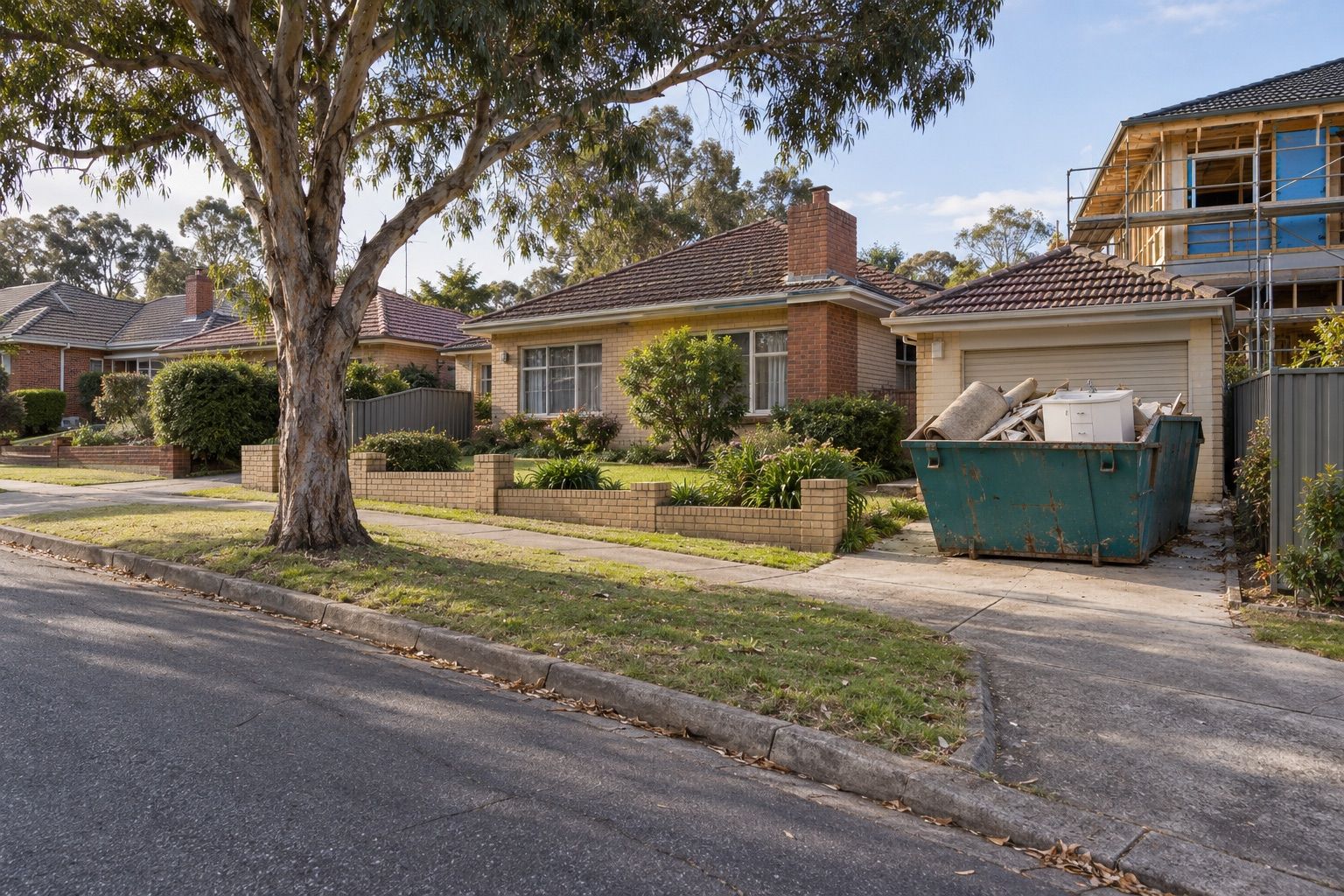 Skip bin hire, Mount Waverley: a teal skip of old carpet and renovation offcuts beside a brick house, a new house being built next door